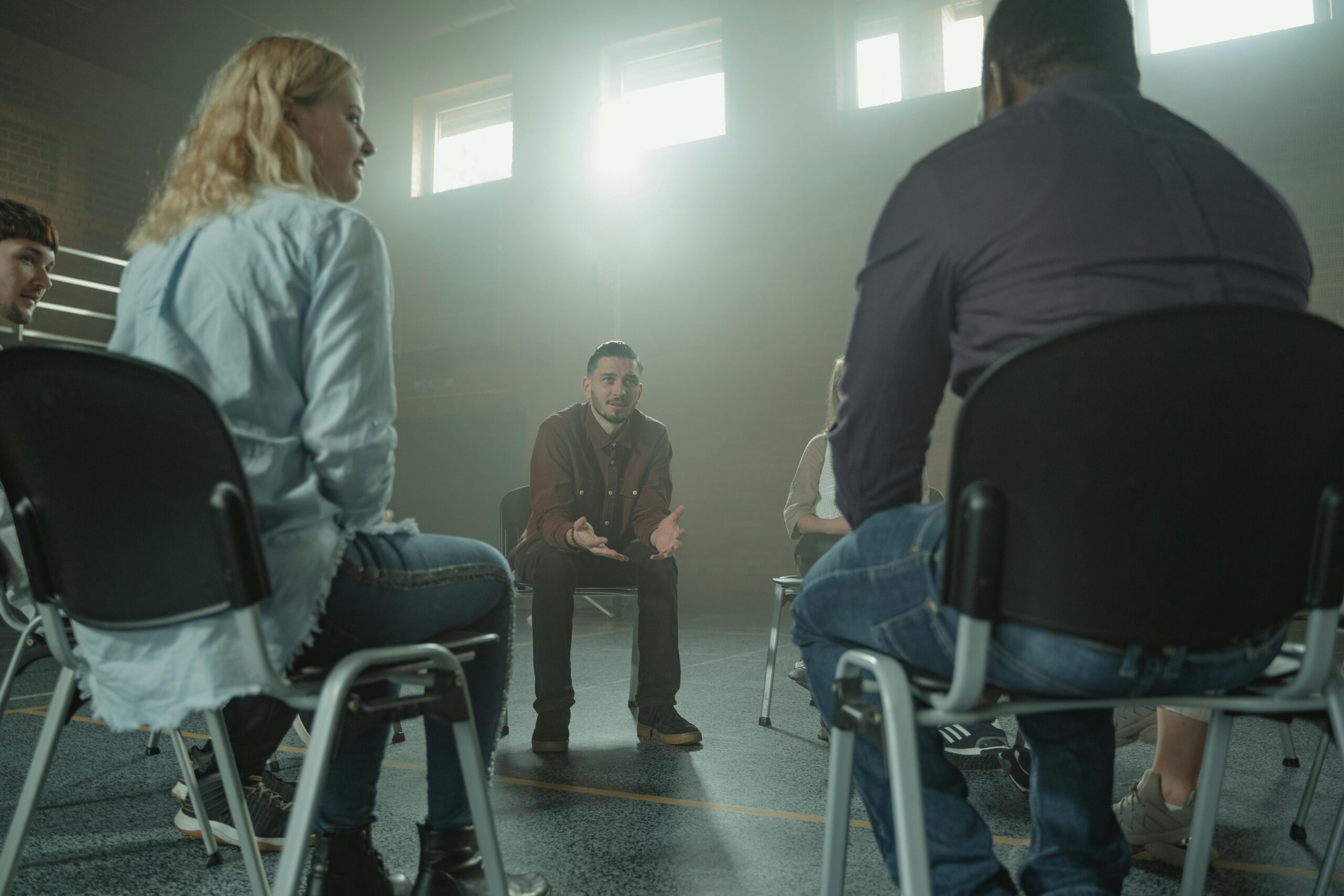 A diverse group of adults in a supportive discussion setting indoors with sunrays.
